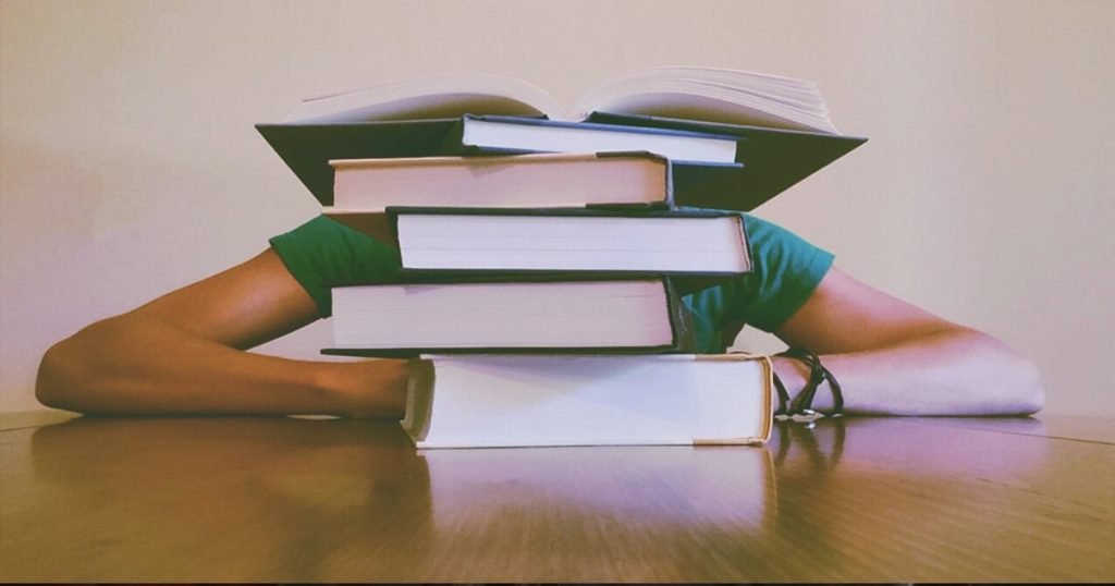 A student fills out a FAFSA application behind a stack of college books.